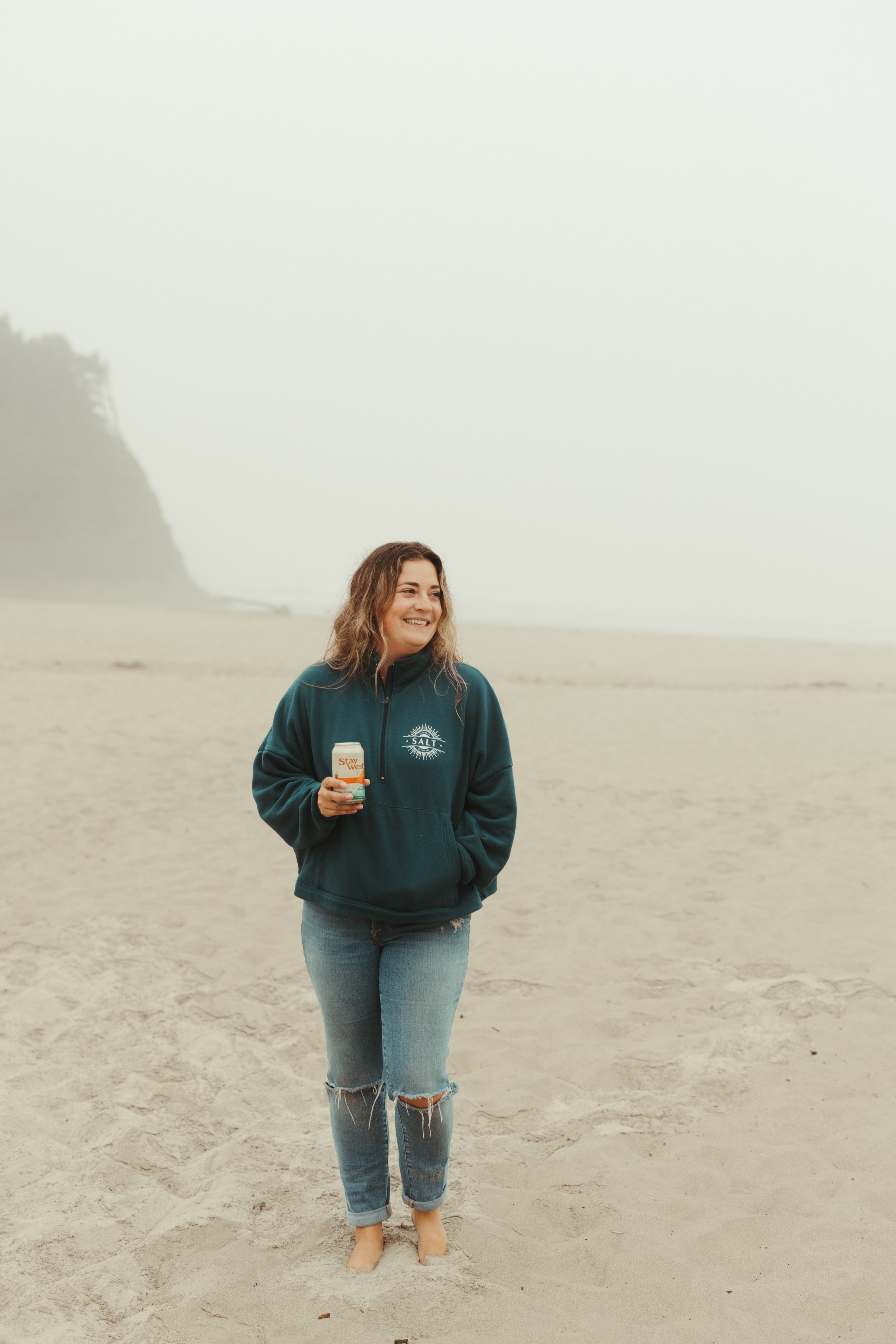 Shelby on the beach holding a can in a Salt half-zip sweater