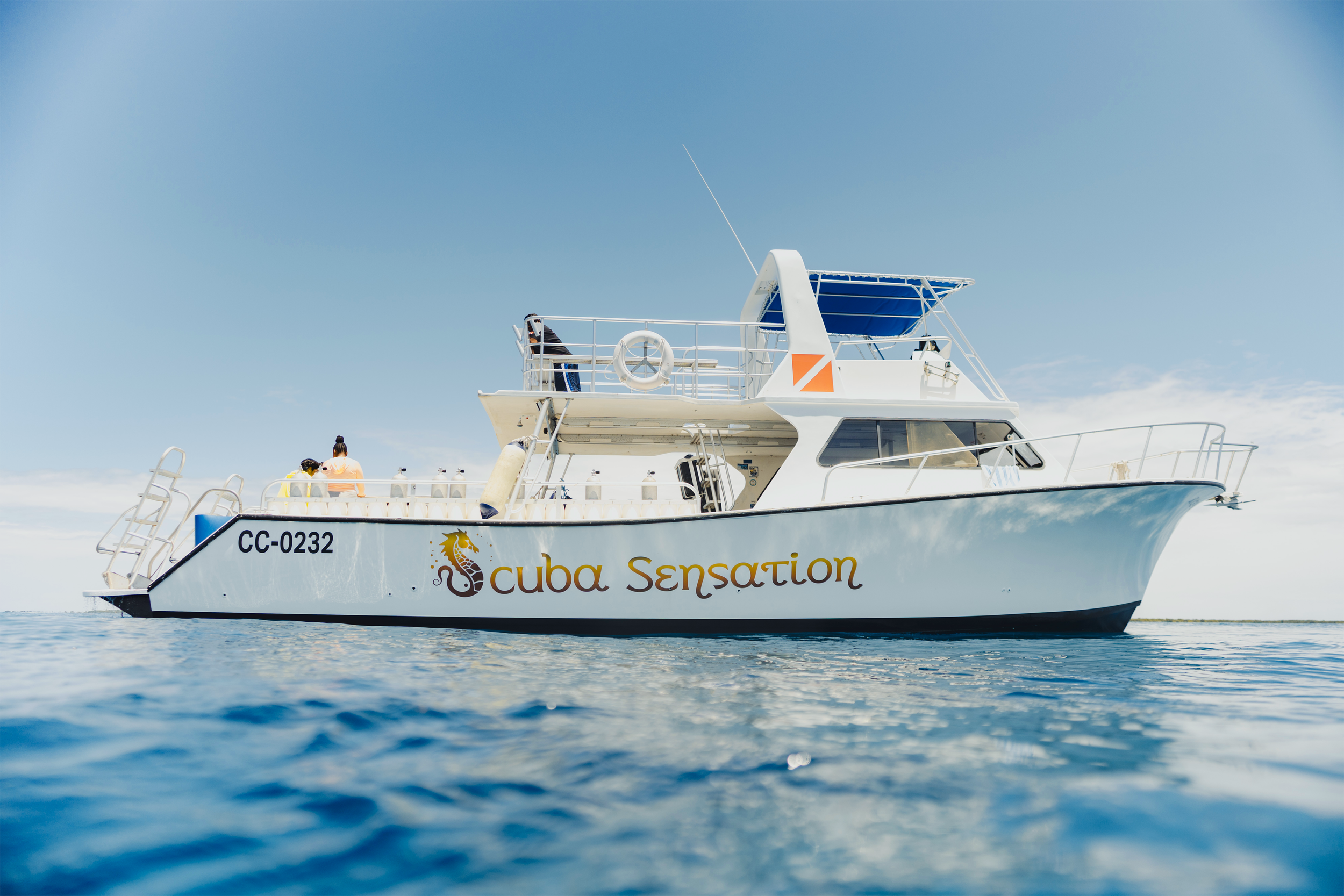 A white boat with the words 'Cuba Sensation' on the side, floating on calm water under a clear blue sky.