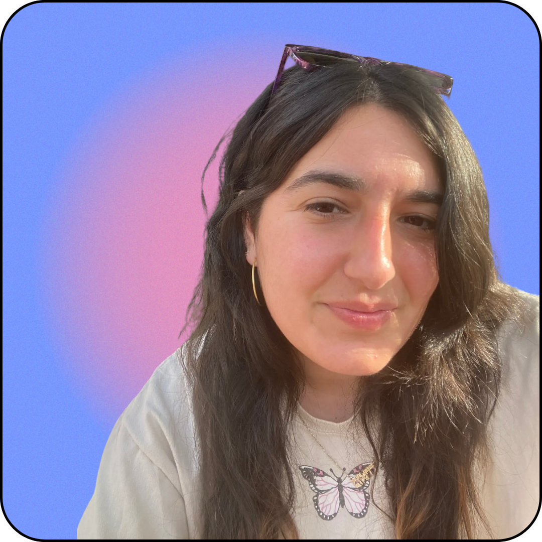 a photo of me, a middle-eastern woman with light brown skin, brown hair, and brown eyes. i'm wearing a beige shirt with a pink butterly, and have purple sunglasses resting on my head.