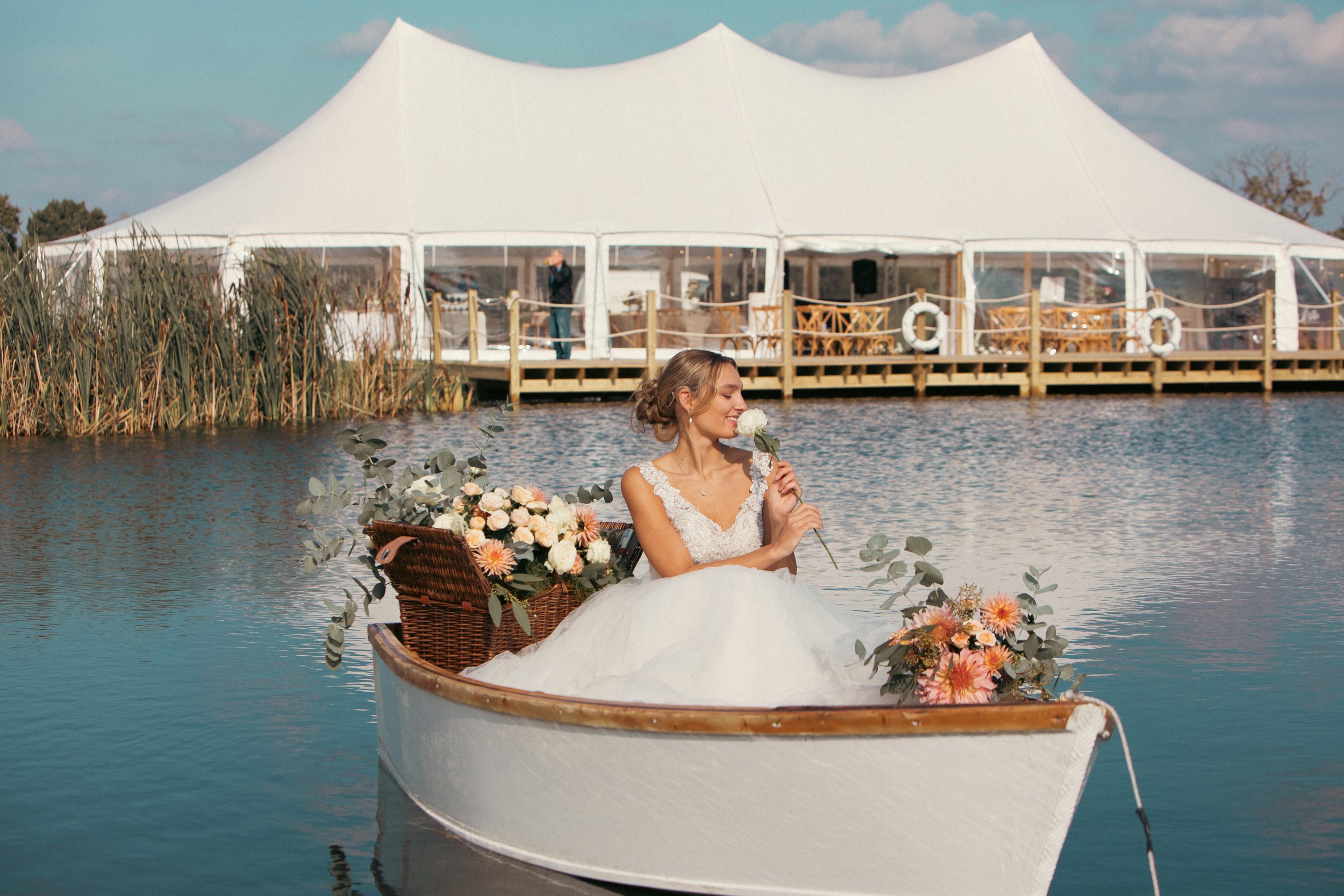 A picture of a traditional pole wedding marquee by St Andrews Lake where a girl in a wedding dress sits in a boat