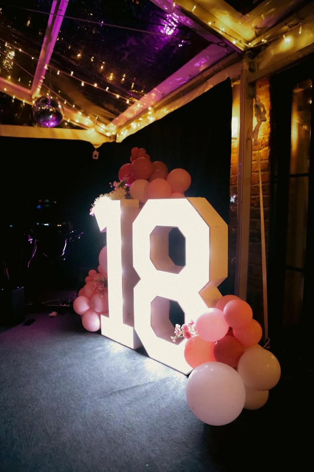 A picture of a clearspan marquee at night decorated with fairylights and disco balls on the roof and an 18th birthday party decoration with pink balloons.