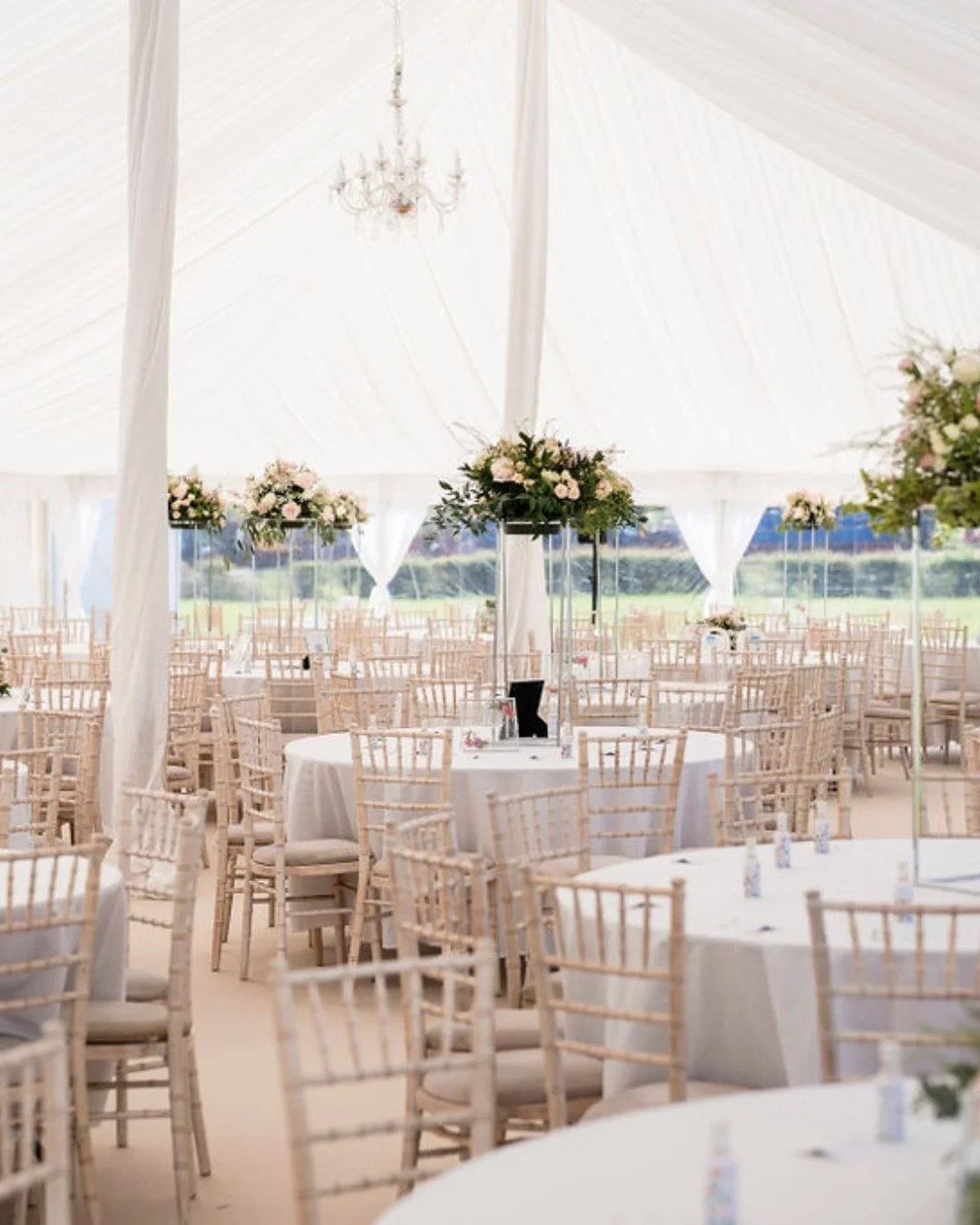A picture of several limewash chiavari chairs around circular tables in a wedding marquee
