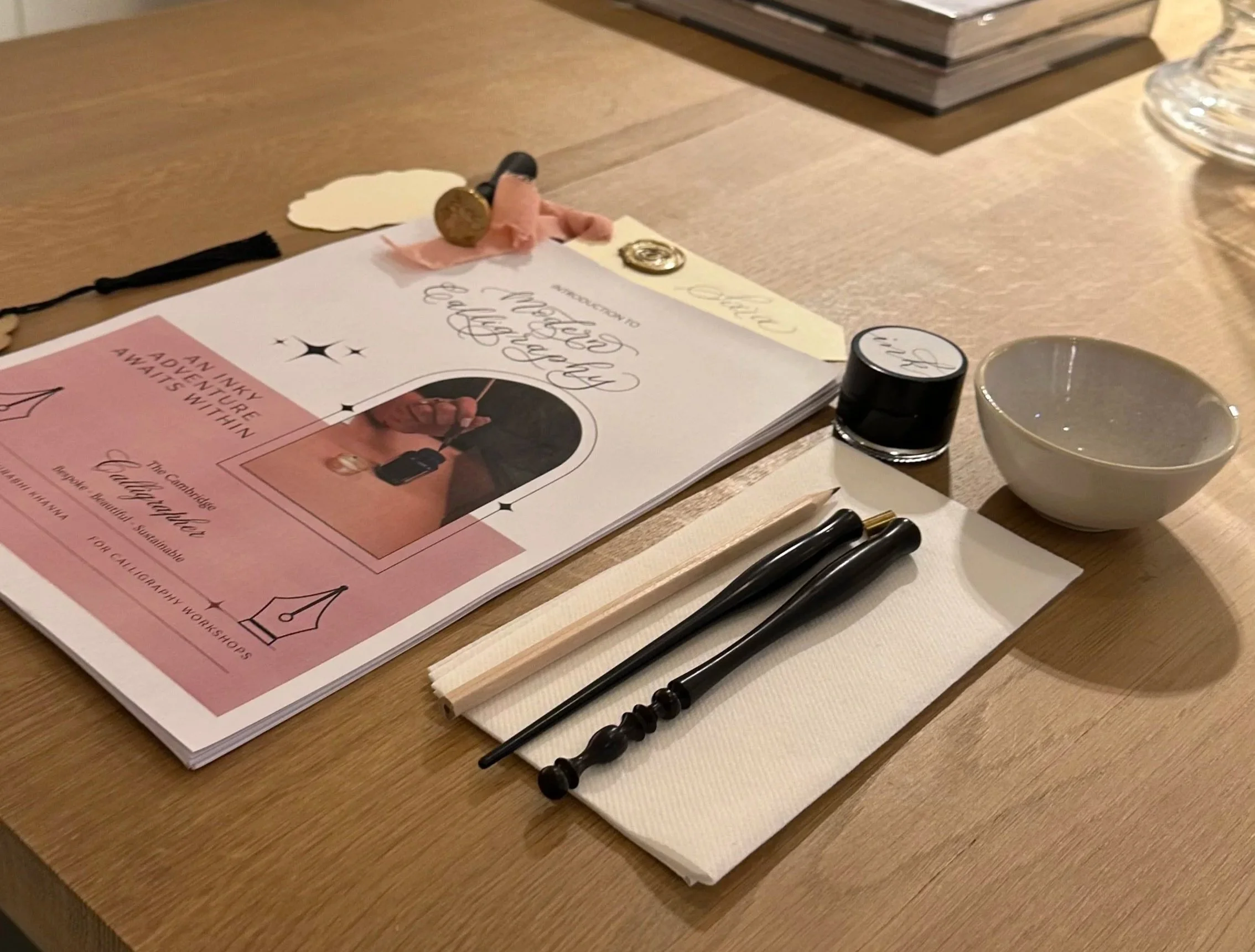 A wooden table set for a calligraphy workshop with a booklet, black ink, a white bowl, a wooden brush, and other calligraphy tools.