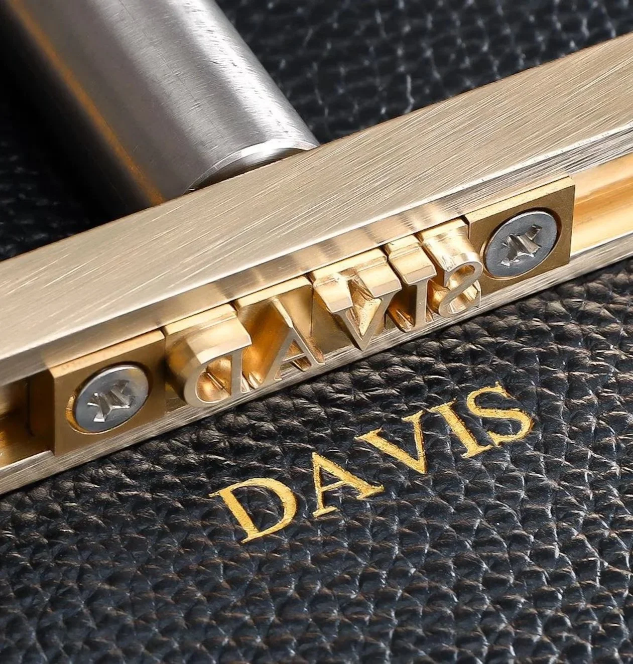 Close-up of a metallic lock with engraved text 'DAYX', placed on a textured black surface with gold lettering 'DAY'S' underneath.