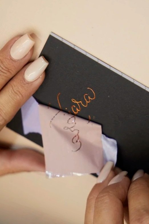 Person peeling off sticker from black notebook with handwritten text visible underneath.