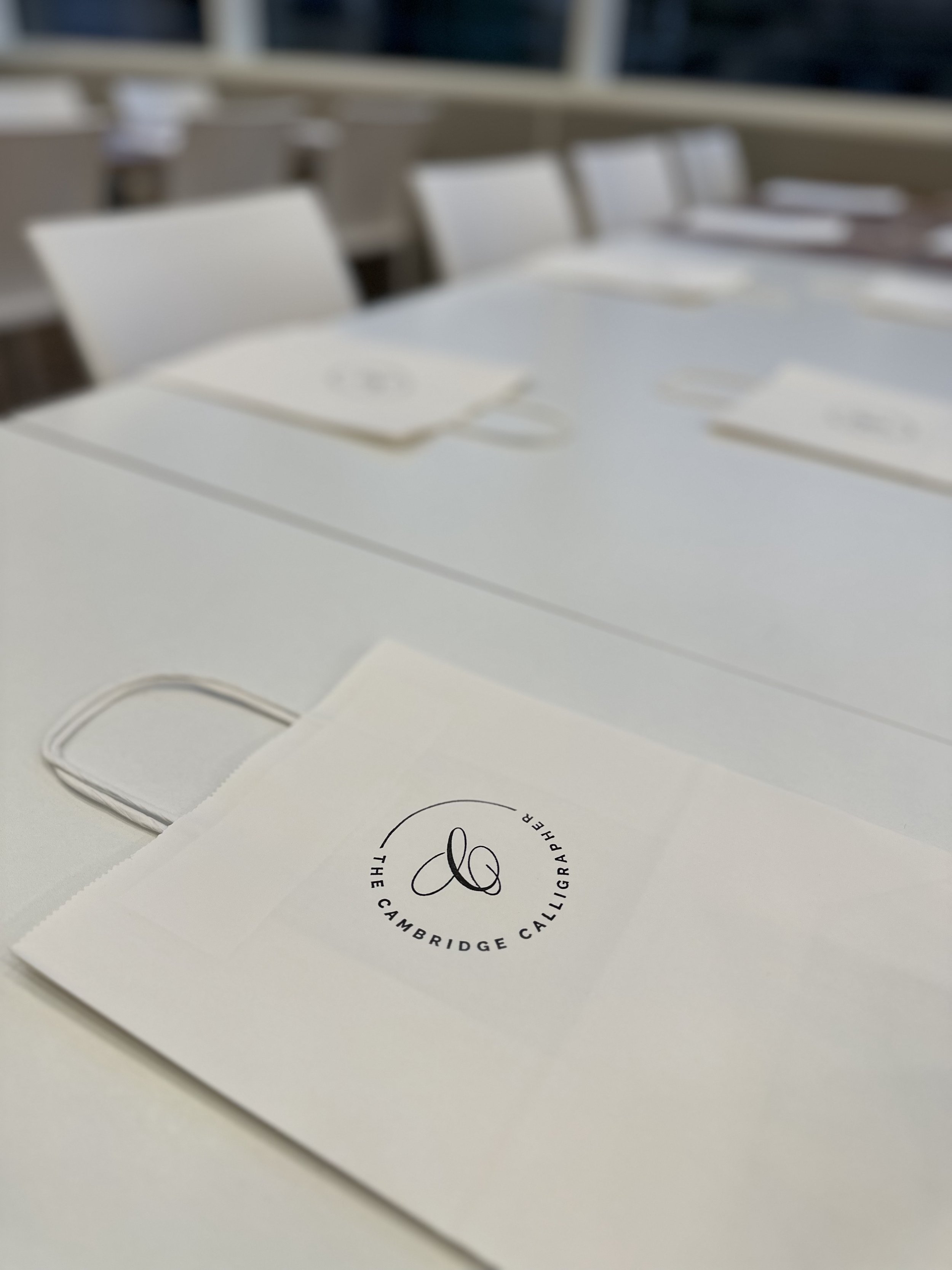 Table setting with white napkins and paper bags featuring a calligraphy logo, in a modern, bright setting.