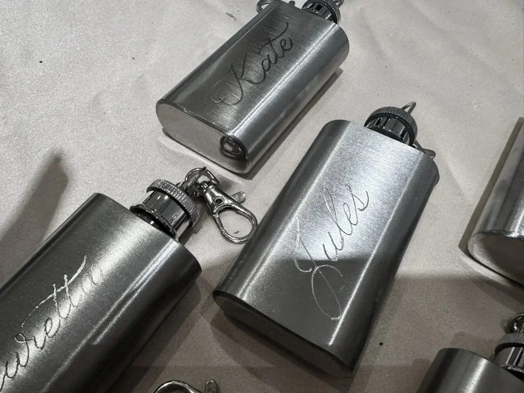 Multiple metallic water bottles with engraved words 'Persistence', 'Faith', and 'Strength' placed on a light-colored surface.