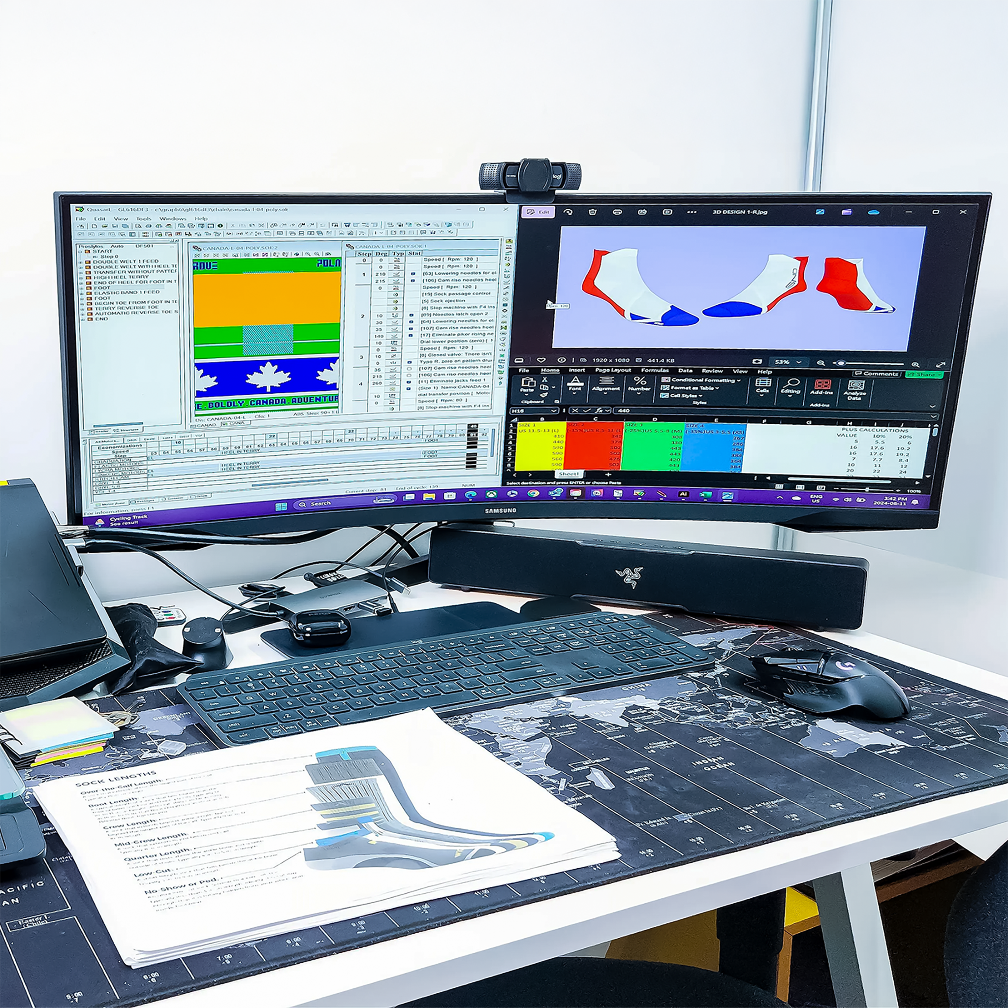A desk with a dual-monitor setup displaying spreadsheets, images, and charts. There are various office supplies, a keyboard, mouse, speaker, and printed documents on the desk.