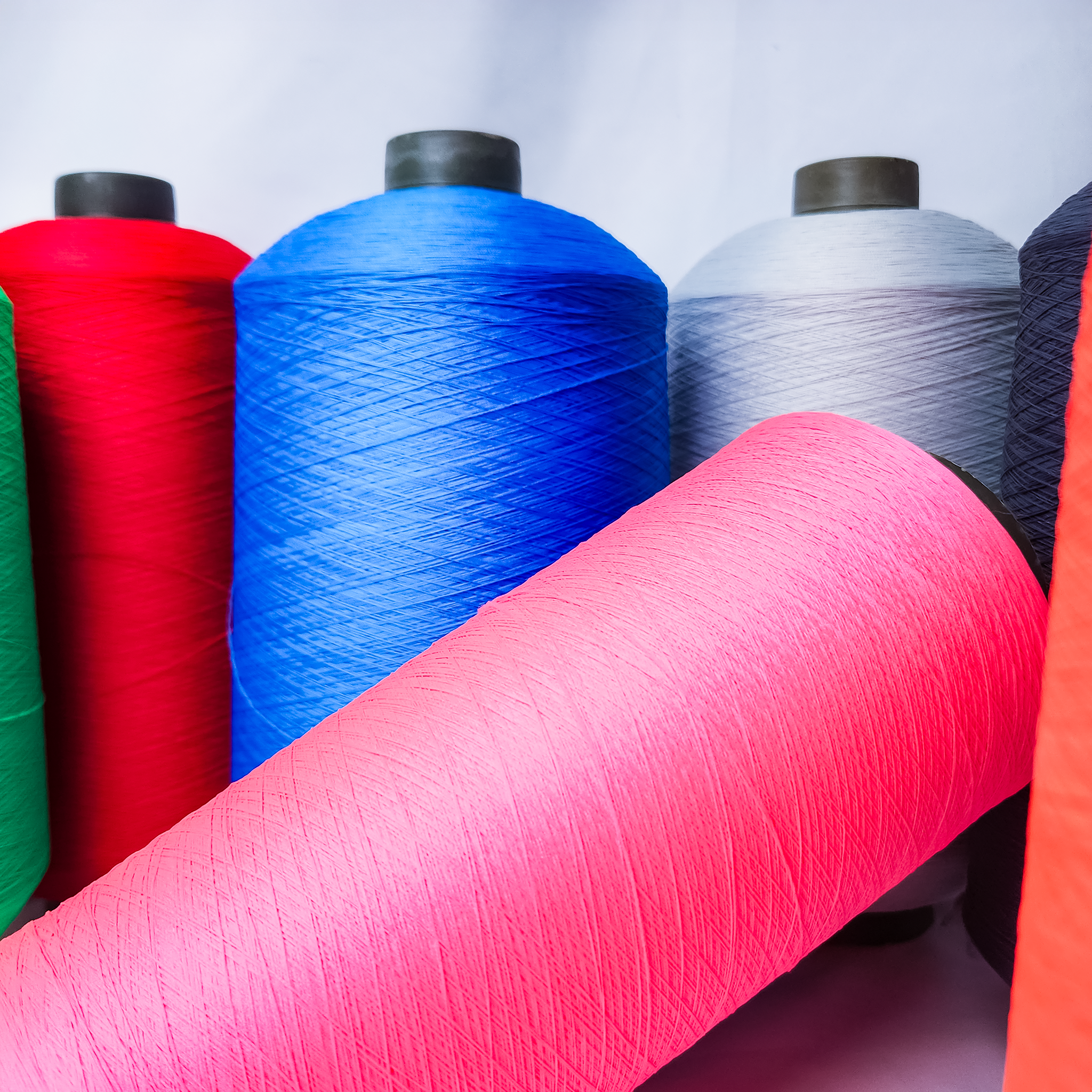 Multiple large spools of thread in various colors, including pink, blue, gray, red, black, and orange, arranged closely together.