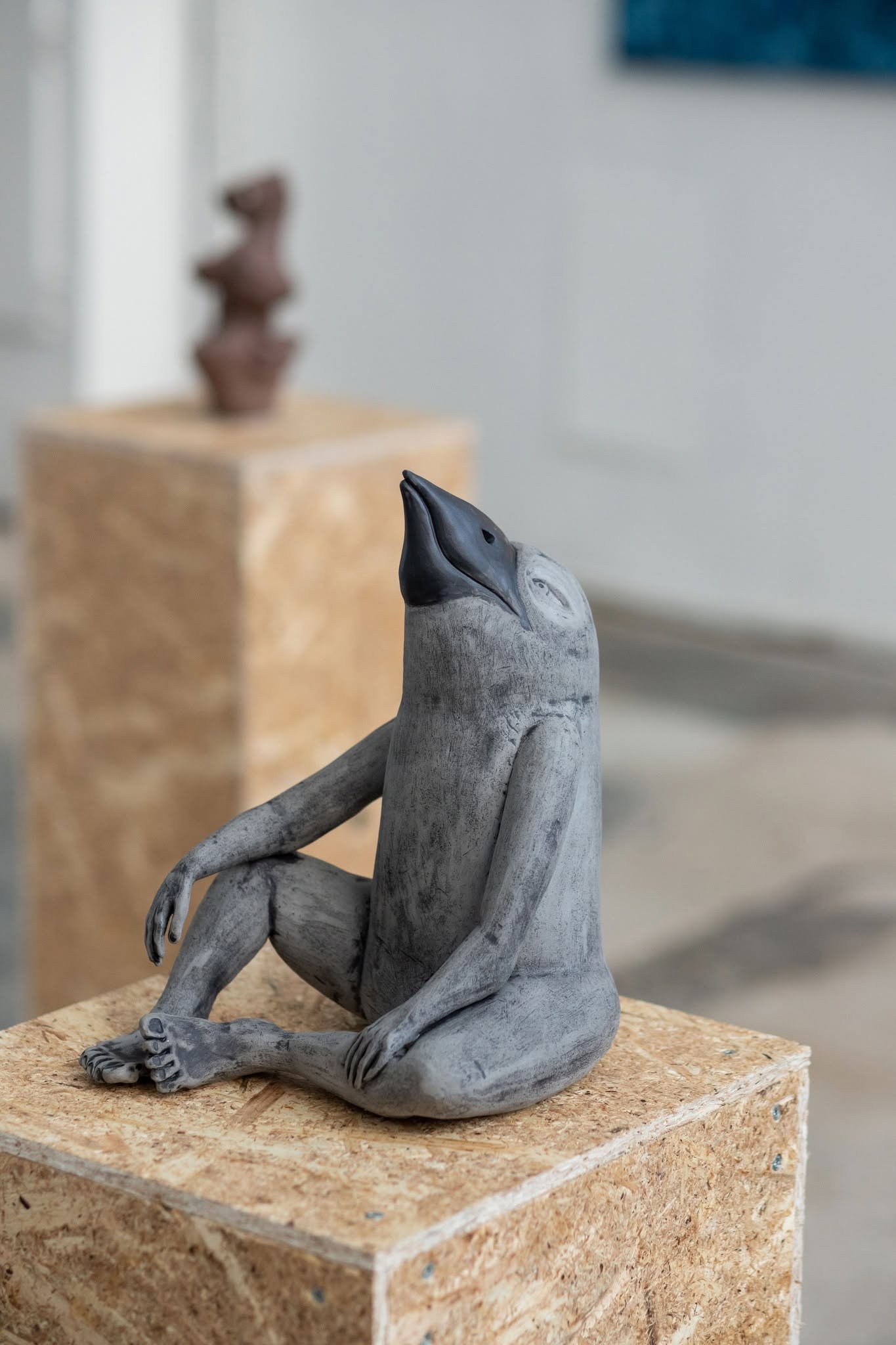 Contemporary ceramic sculpture on a pedestal displayed in the the exhibition SPACETIME  UN[B]LOCKED, featuring human-like bird created by Monika Dombrauskytė.