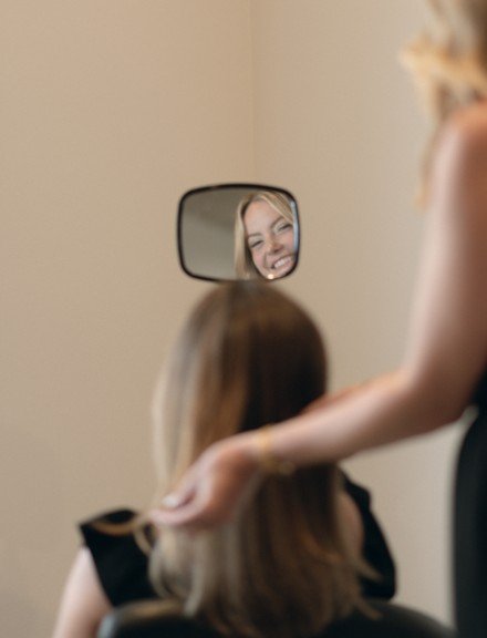 Person looking in a mirror with a woman's face reflected in the mirror, smiling at new trendy hair.