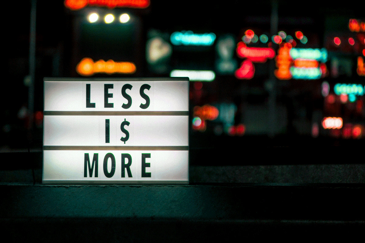 Illuminated sign reading “Less is More” with a dollar sign, symbolizing minimalist efficiency and the value of doing more with less in modern work culture.