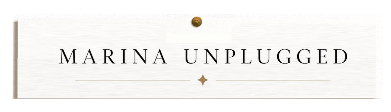 Close-up image of a sign that says 'Marina Unplugged' in black letters on white background with gold accents.