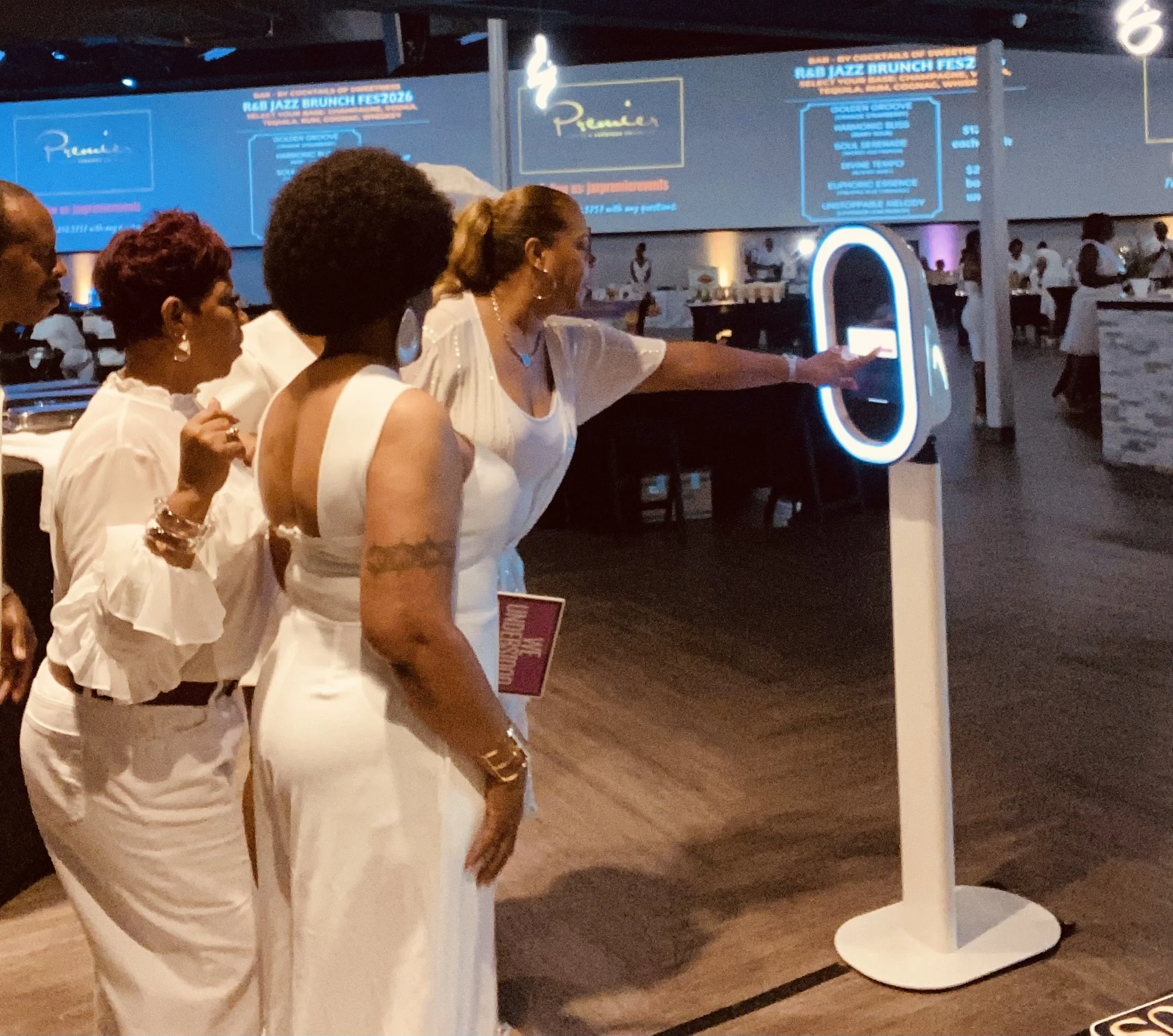 People sitting at a table in a restaurant or event space, with a blue digital menu board for a jazz brunch event visible in the background.