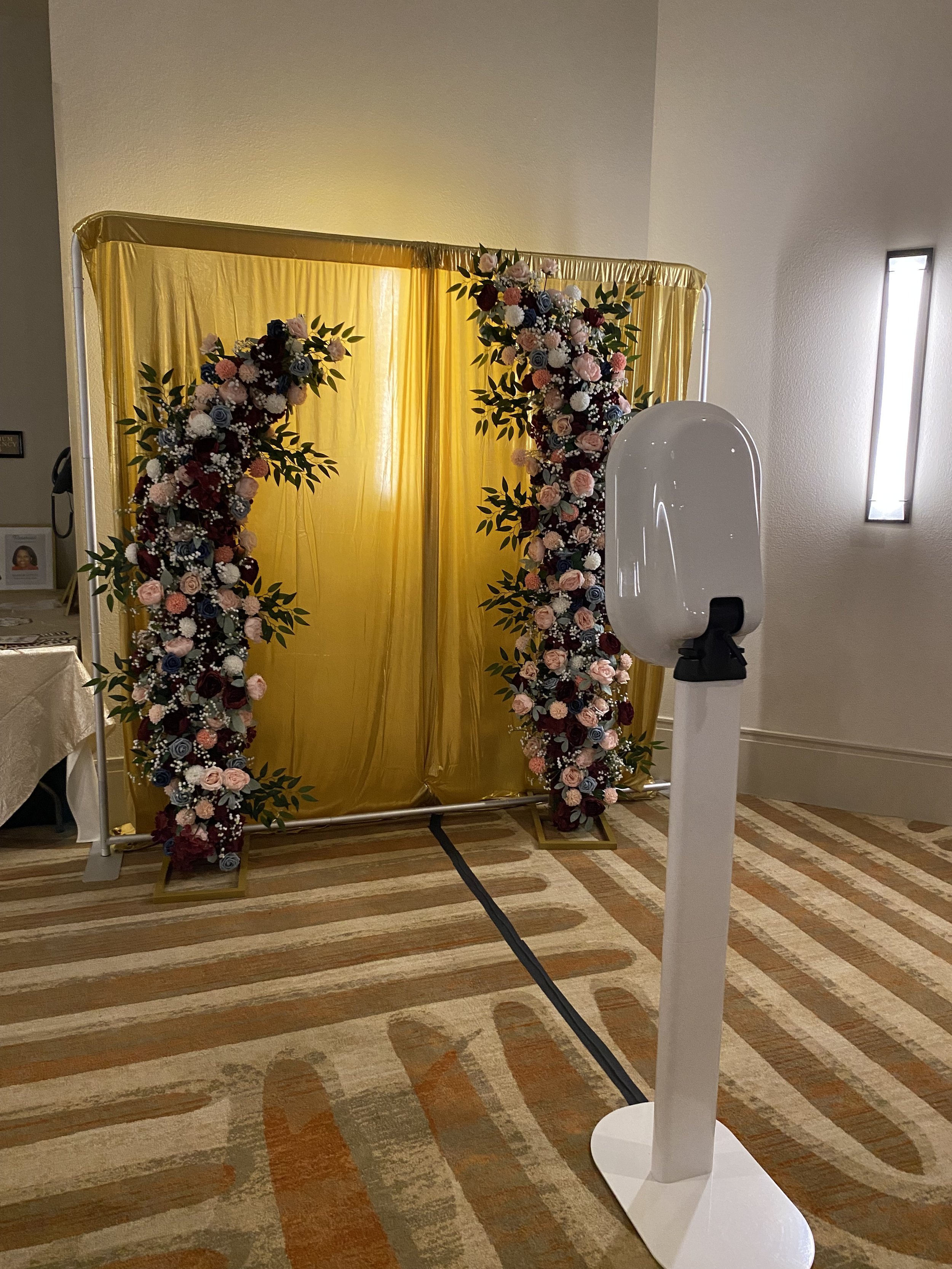 Decorative wedding backdrop with a yellow curtain and floral arrangements on standees with pink, white, and purple flowers, and green leaves.