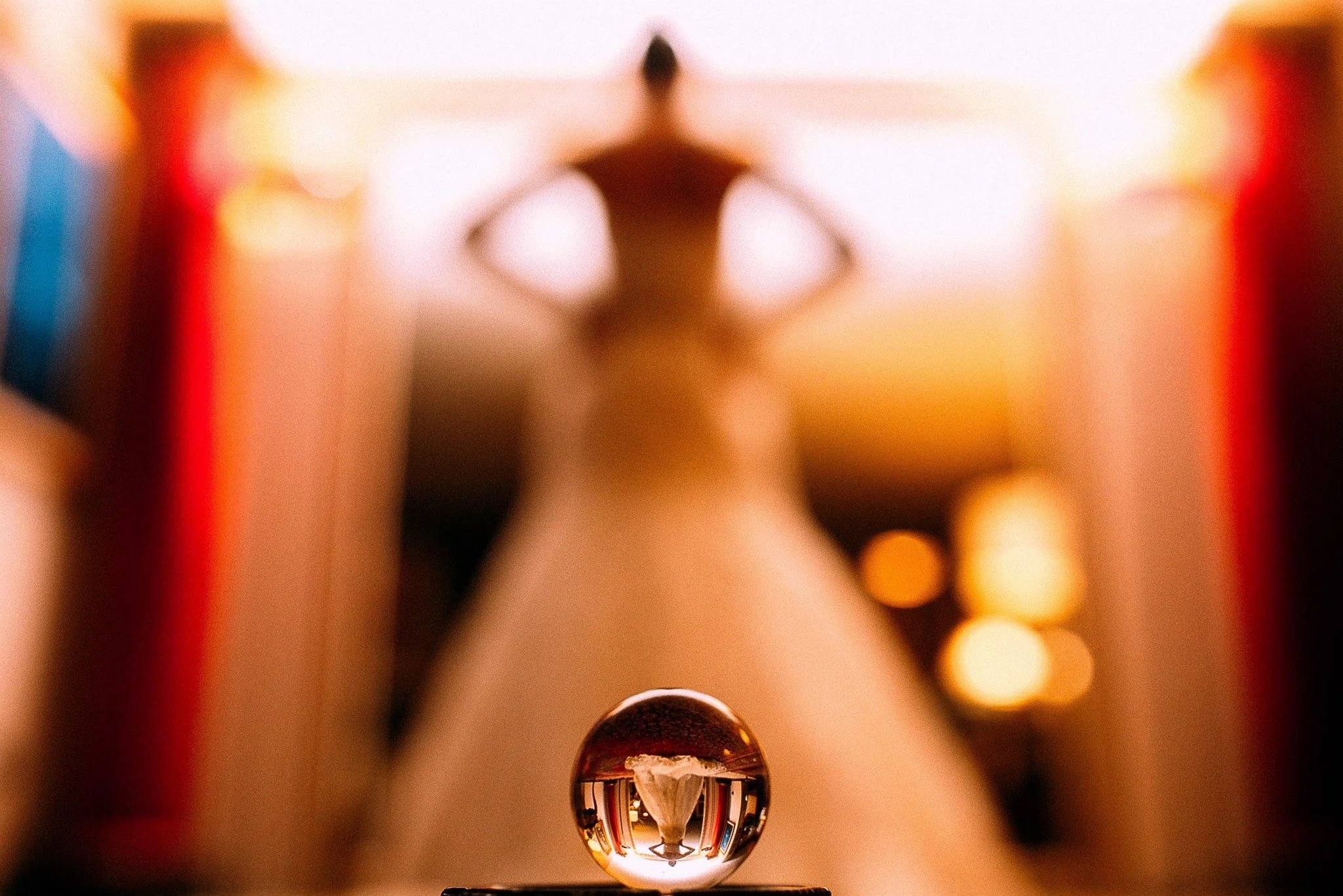 Close-up of a metallic ball bearing on a workbench, with a person and colorful objects reflected in the shiny surface.