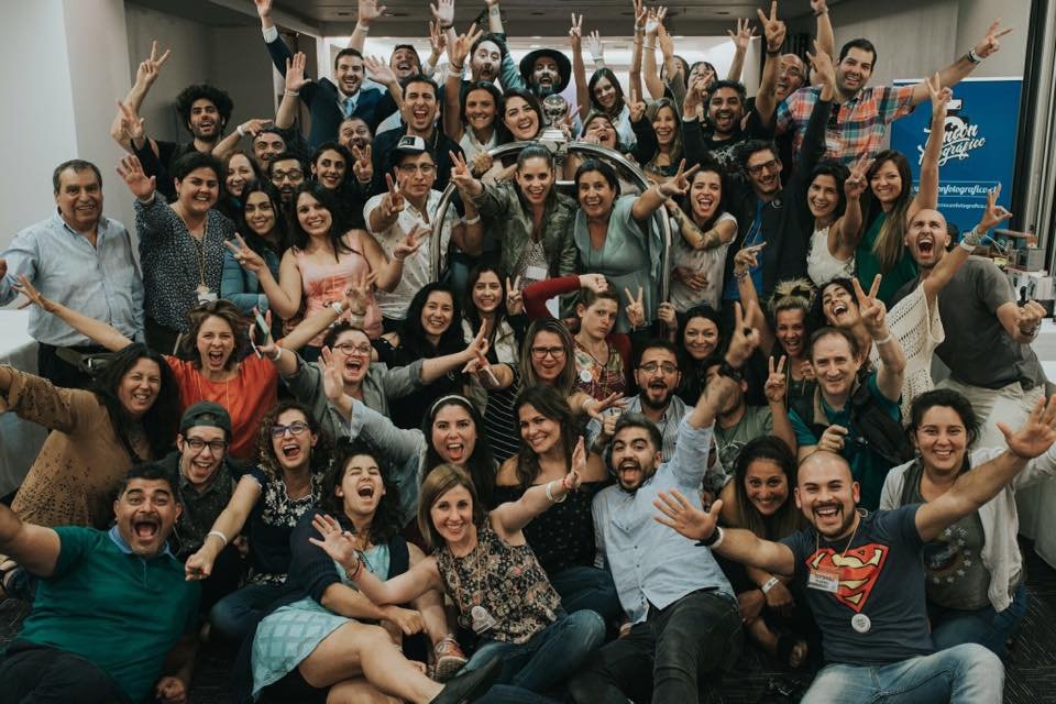 Group of diverse people indoors, smiling, laughing, and making peace signs for a group photo.