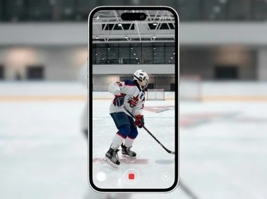 A person playing ice hockey is visible through a smartphone screen, on an ice rink.
