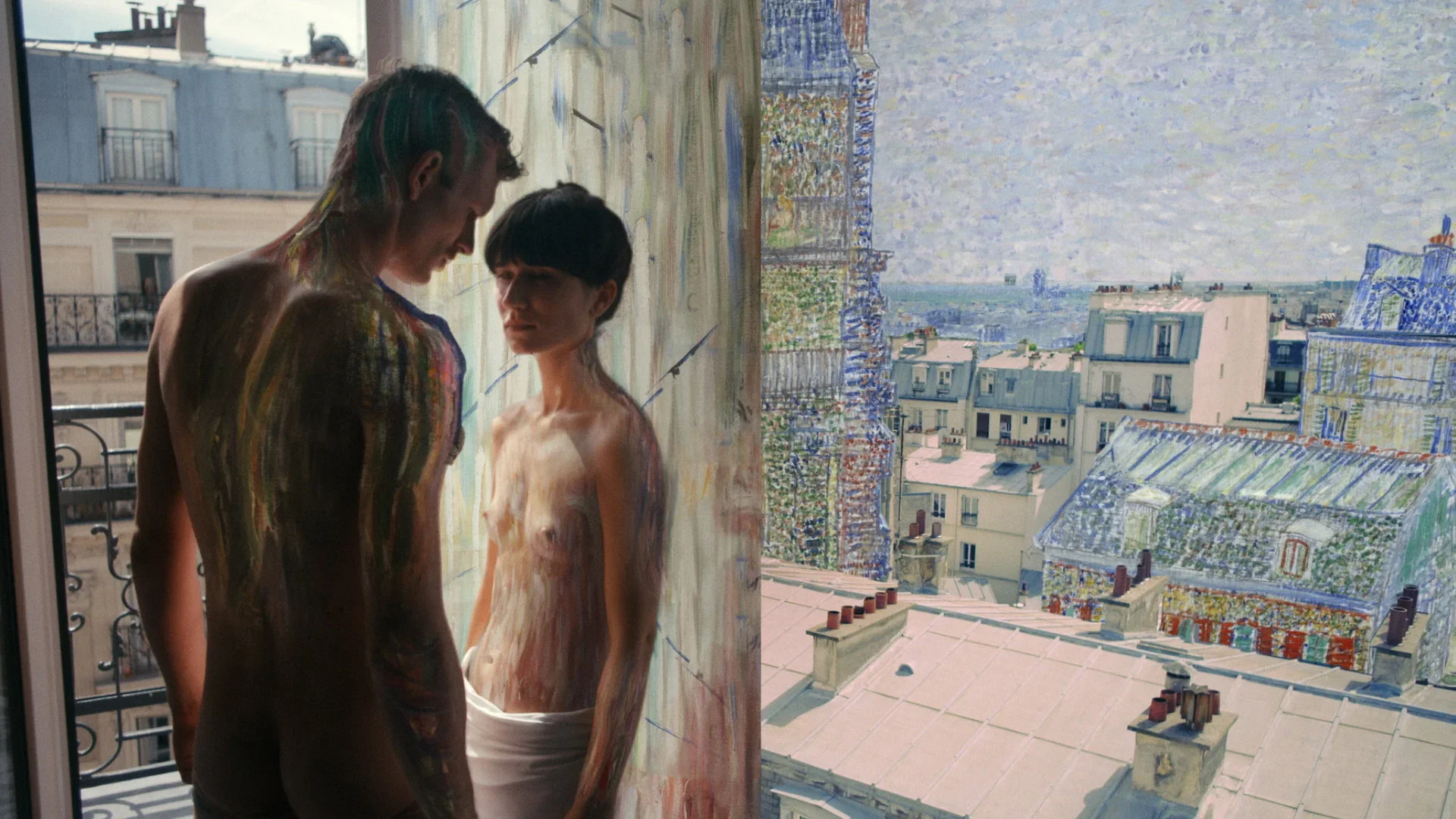 Two people, one with rainbow-colored hair, are standing close to each other near a window with a cityscape view in the background, with paint on their skin, in an urban apartment.