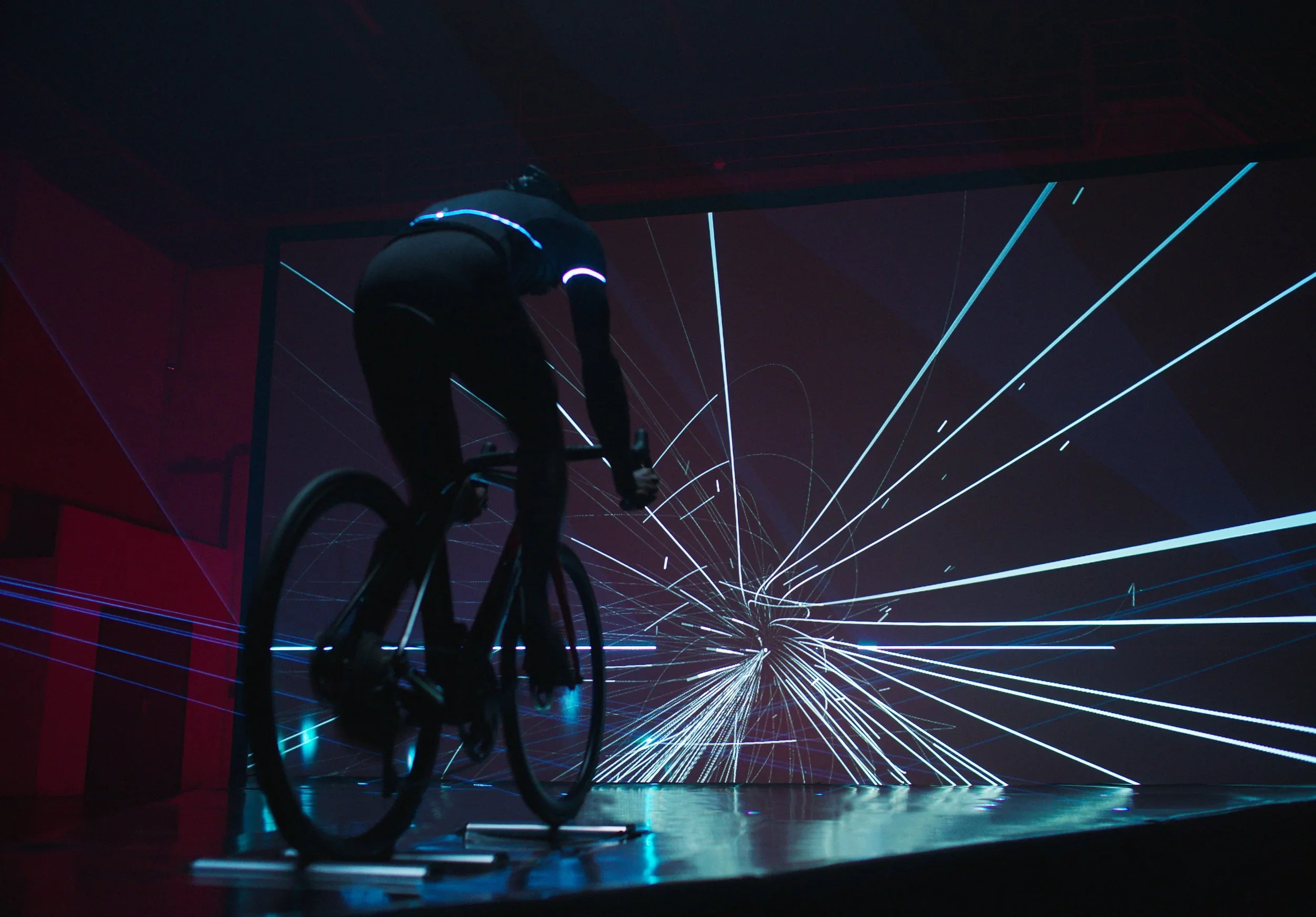 A person riding a bicycle in front of a digital, space-themed background with lines and light bursts.