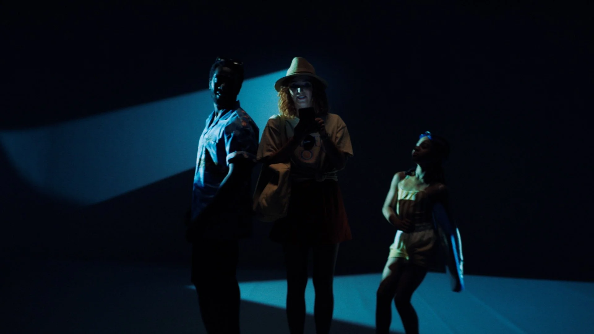 Three people standing in a dark space illuminated by a blue spotlight.
