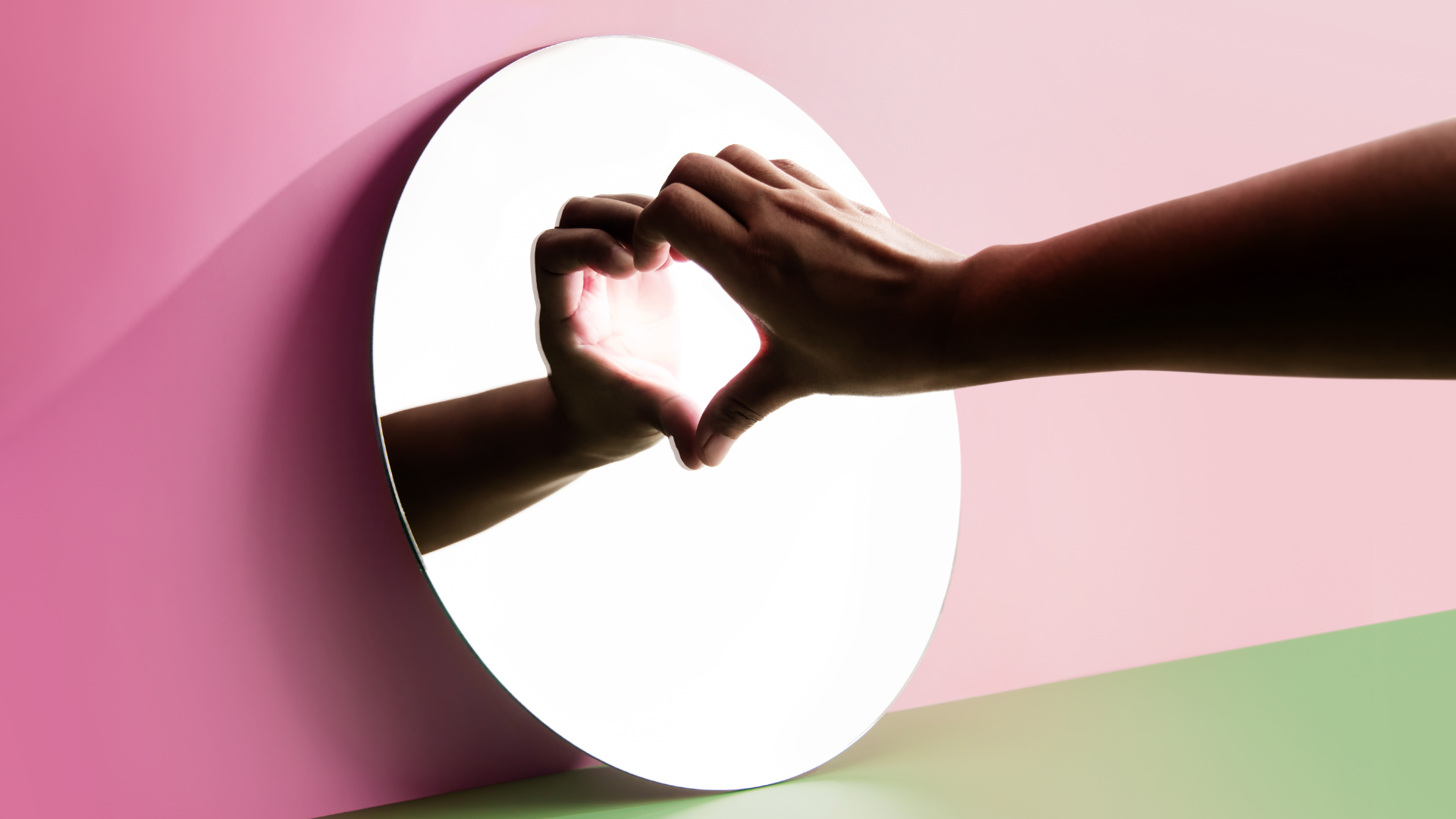 A person making a heart with their hands in a mirror