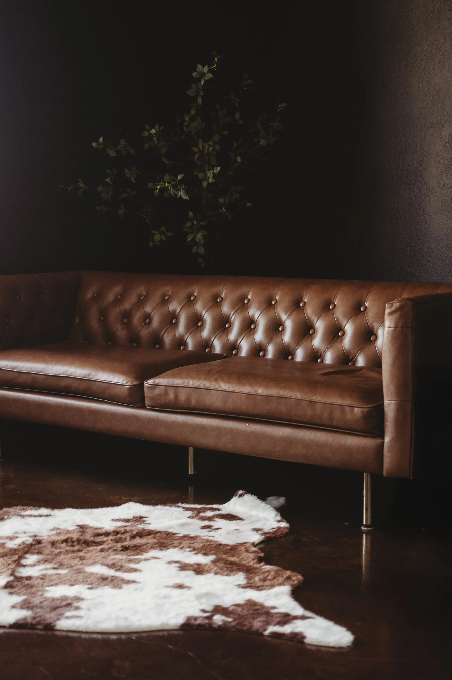 Classic brown leather Chesterfield sofa and cowhide rug on the dark moody side of our photography studio rental in D'Iberville MS.
