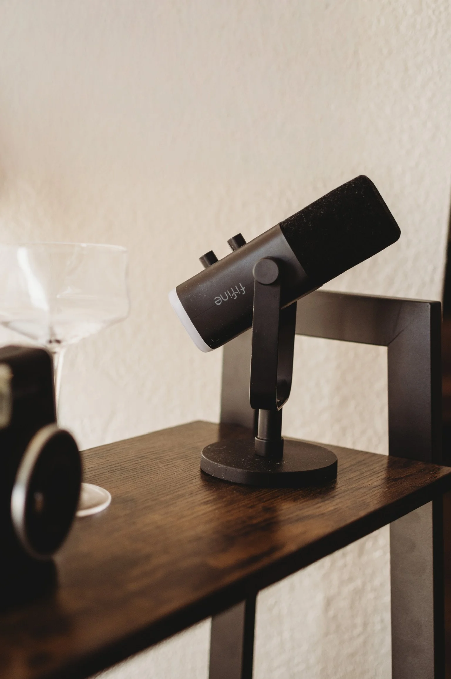 A black and gray FiiT microphone on a wooden table next to a clear martini glass,  Vintage black camera and carved wooden decor props available for styling at our lifestyle photography studio rental in D'Iberville MS.