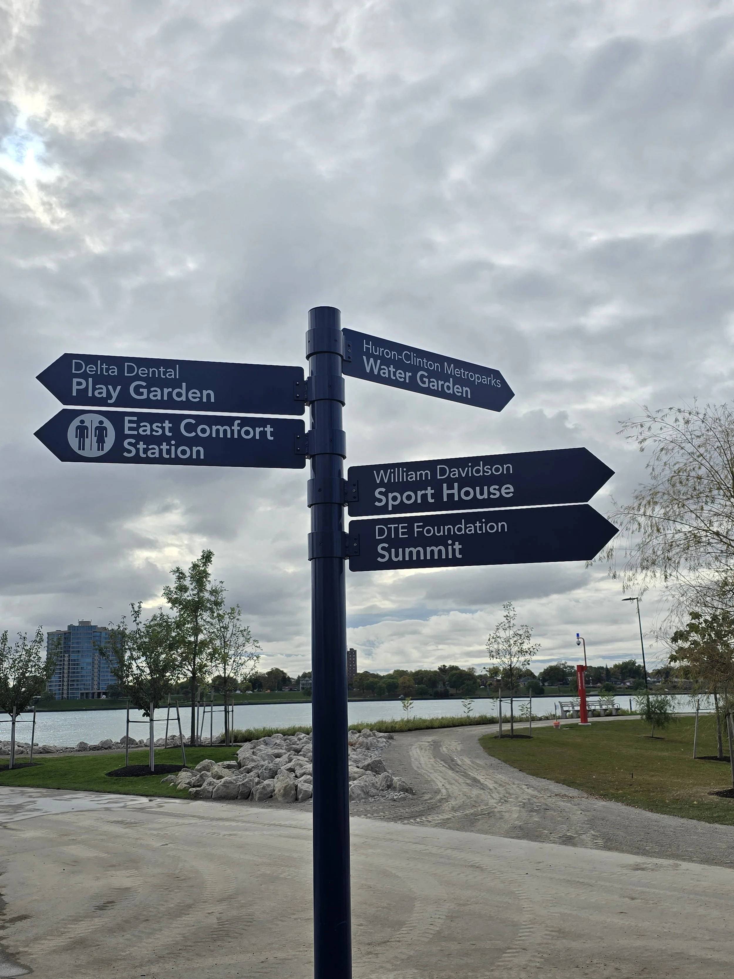 Directional signpost near a waterfront with trees and residential buildings in the background.