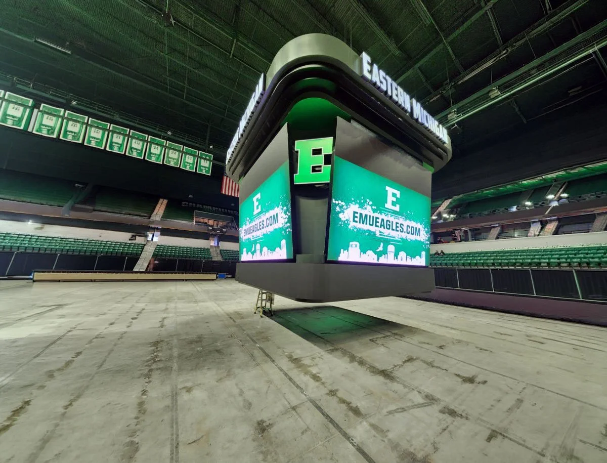 Large digital scoreboard displaying the logo for Eastern Michigan University, with green and white colors, and seating in the background.