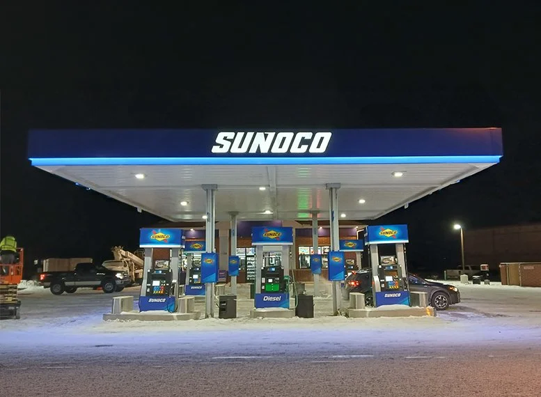 Sunoco gas station canopy and illuminated signage at night with multiple fuel pumps and vehicles.