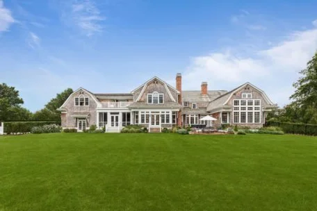 Large house with multiple gables and a spacious lawn under a partly cloudy sky.