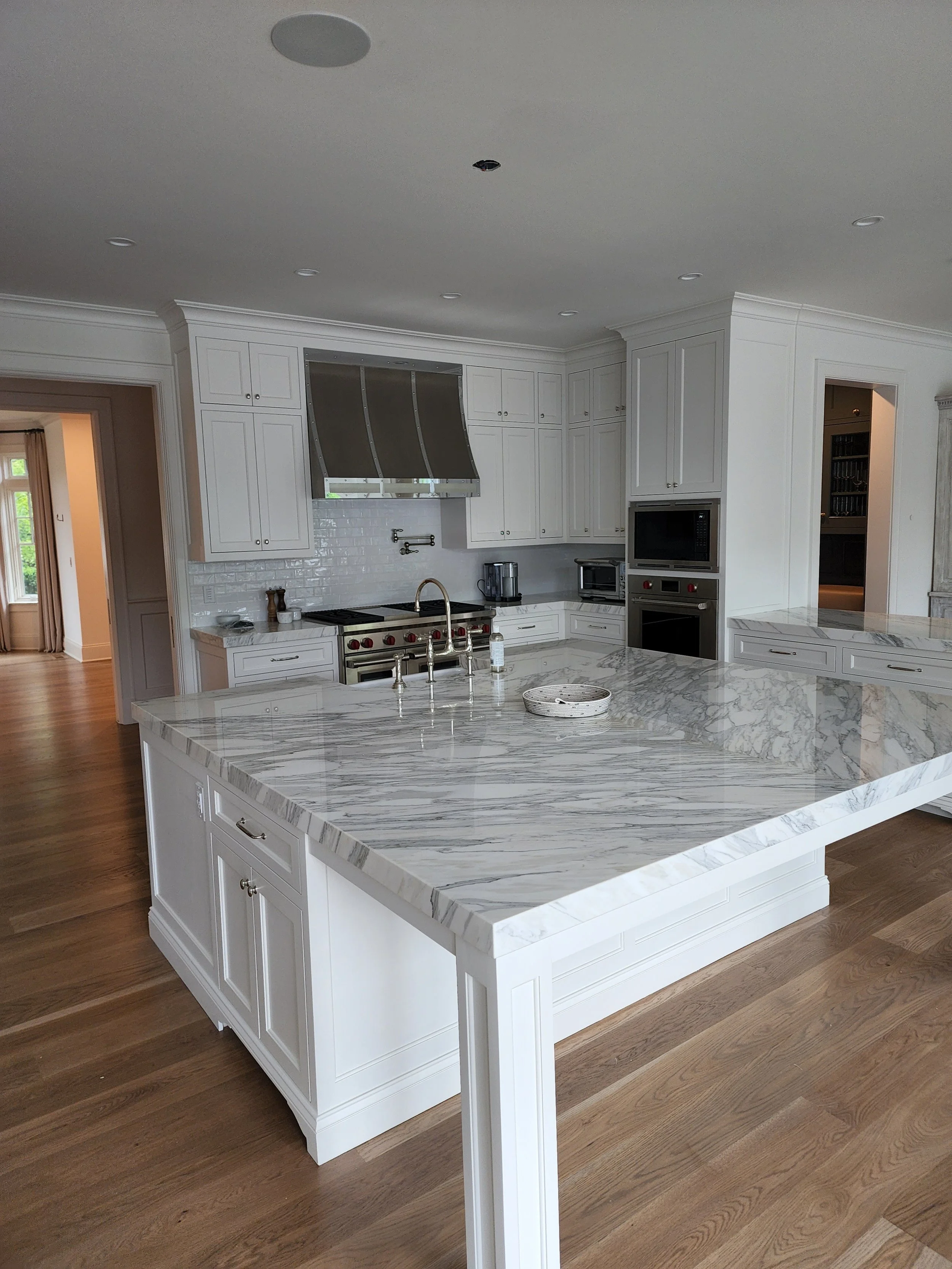 Modern white kitchen with marble countertop island and wooden flooring.