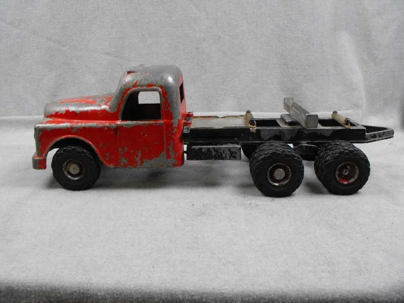 A vintage toy truck with a red and silver cabin, black chassis, and six black rubber wheels.
