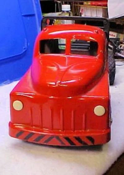 A red miniature fire truck toy with a black ladder and yellow headlights, placed on a white surface.