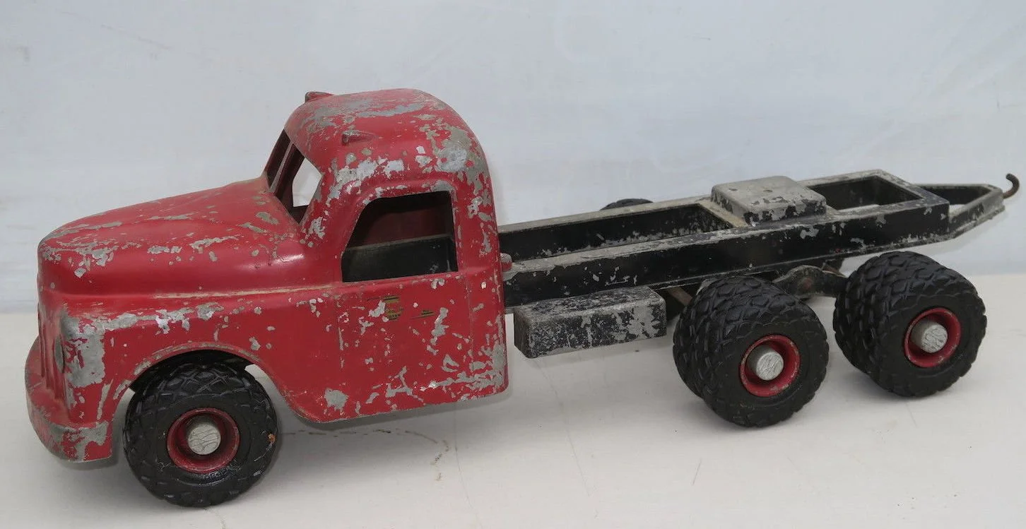 Vintage toy pickup truck with a red cab, black flatbed, and four black tires, showing signs of paint chipping and wear.