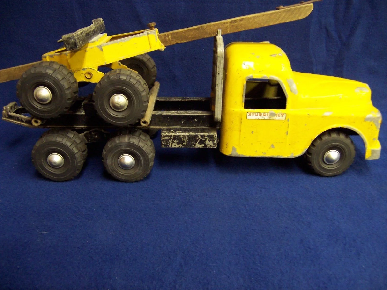 Yellow toy tow truck with a smaller toy bulldozer on its flatbed, placed on a blue surface.