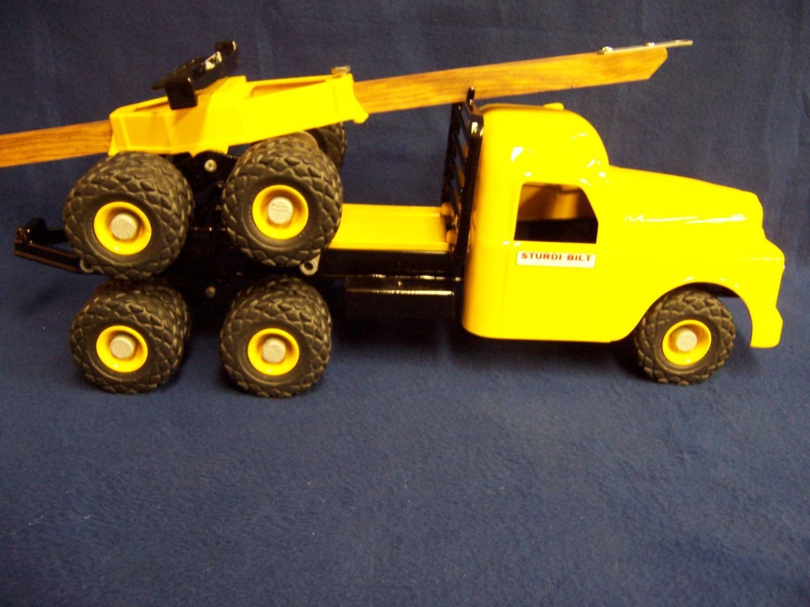 Yellow toy truck with a flatbed carrying a toy forklift and six large black wheels.