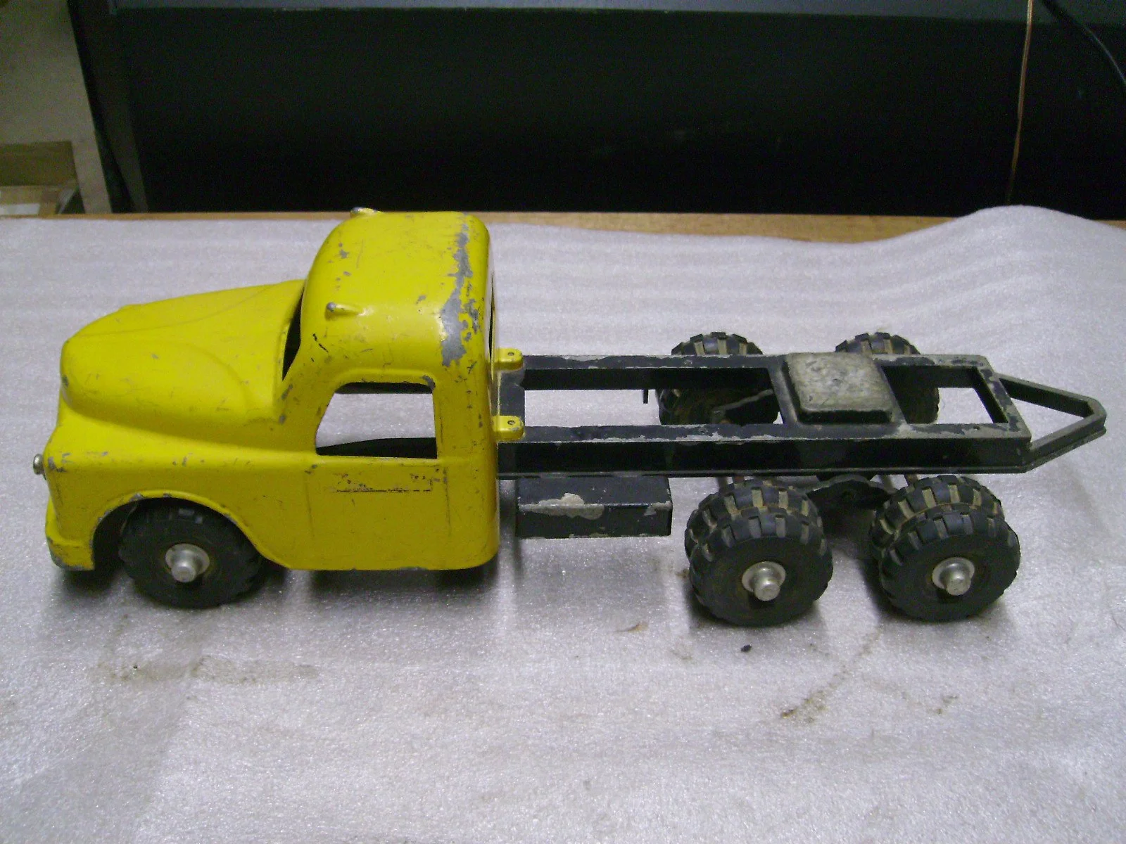 A vintage yellow toy tow truck with black wheels on a white surface.