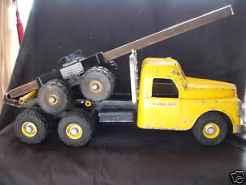 A toy yellow truck with black wheels and a long wooden plankt attached to its bed.