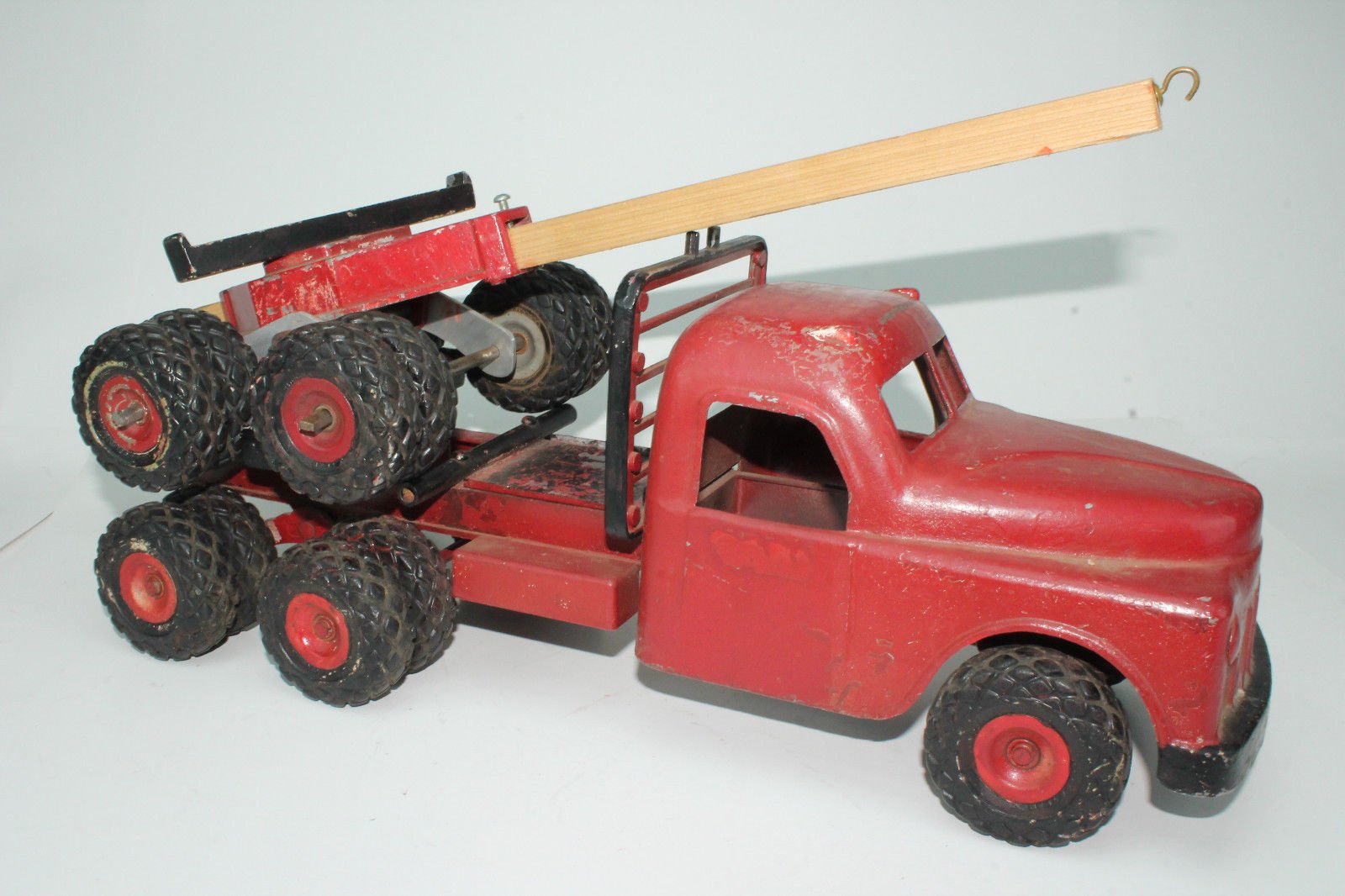 A vintage red toy tow truck with large black wheels, a flatbed, and a wooden boom with a hook.