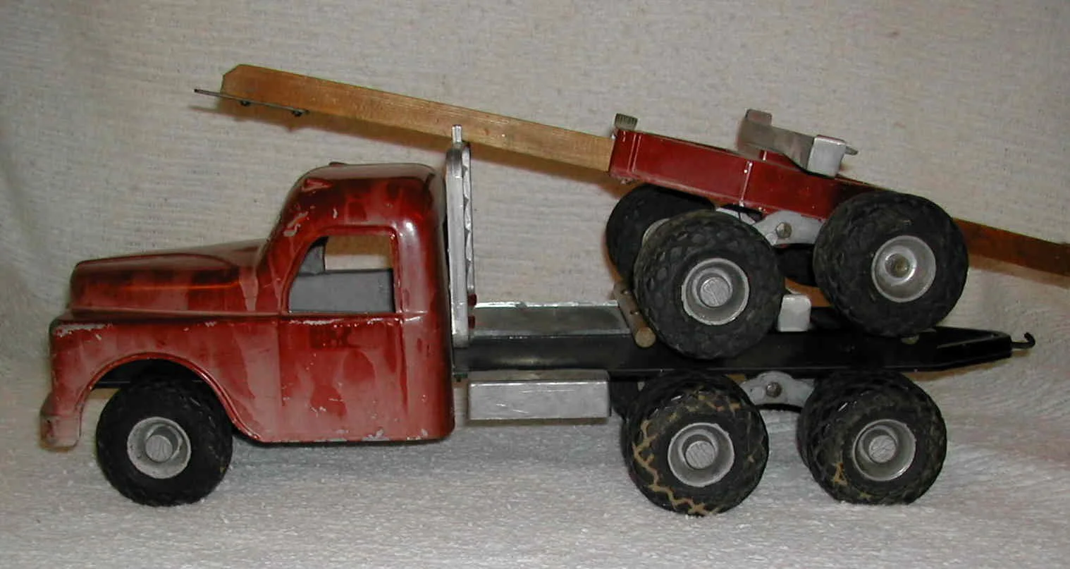 A vintage toy red tow truck with a flatbed and a wooden crane arm on a light-colored textured background.