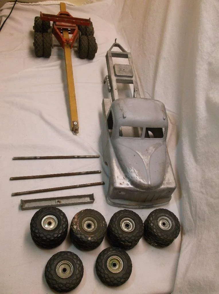Disassembled toy car, four small rubber tires, four metal axles, two metal rods, a metal frame, and a plastic chassis on a white sheet.