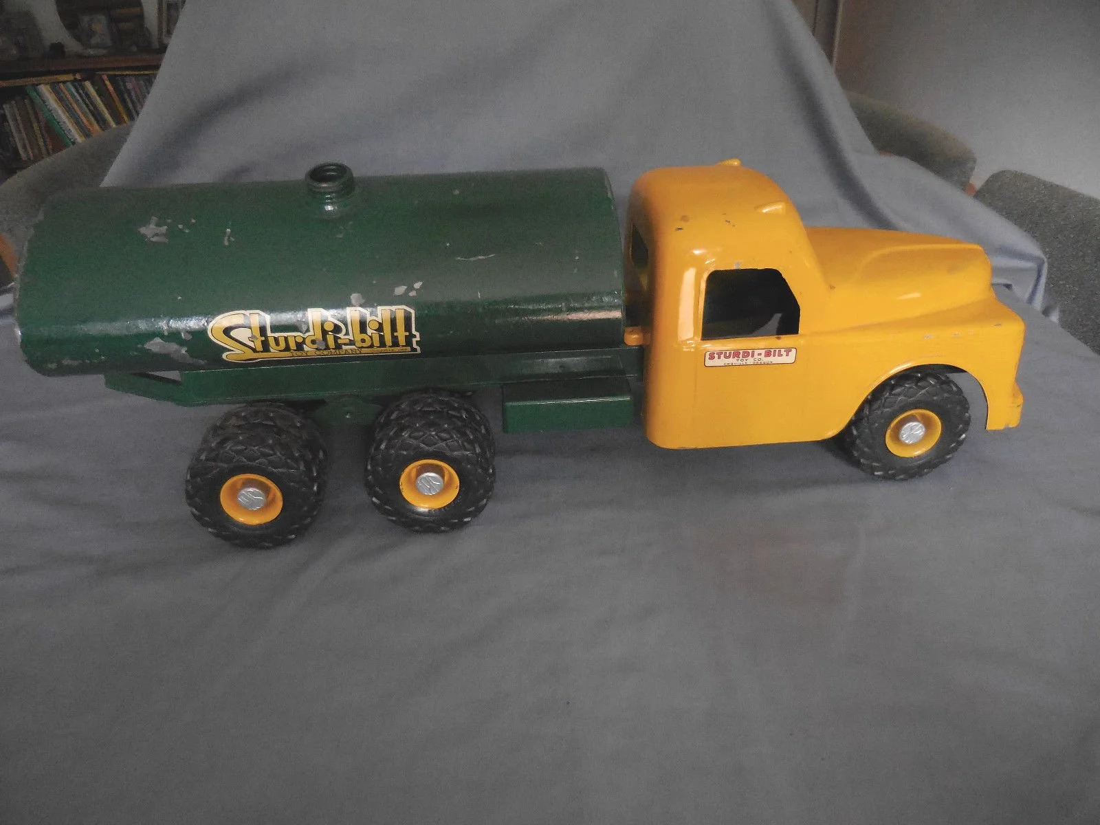 A vintage Sturdi-Bilt toy truck with a yellow cab and green tank, six black wheels with yellow centers, and a logo on the side.