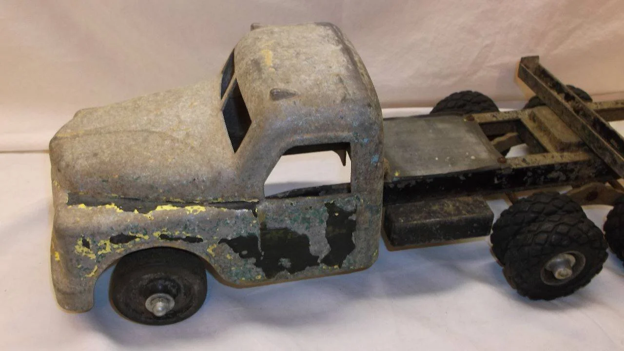An old, rusty toy truck with a flatbed and towing wheels, showing signs of corrosion and paint chipping.