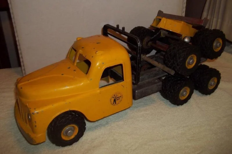 Yellow vintage toy truck with black tires and a second smaller toy car placed on top of it.