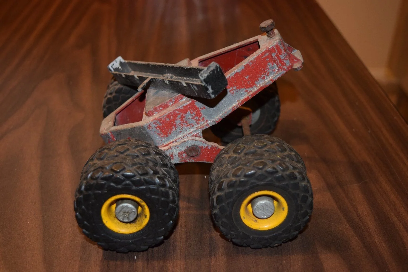 A small, vintage toy truck with four large, textured black tires and yellow hubcaps, on a wooden surface.