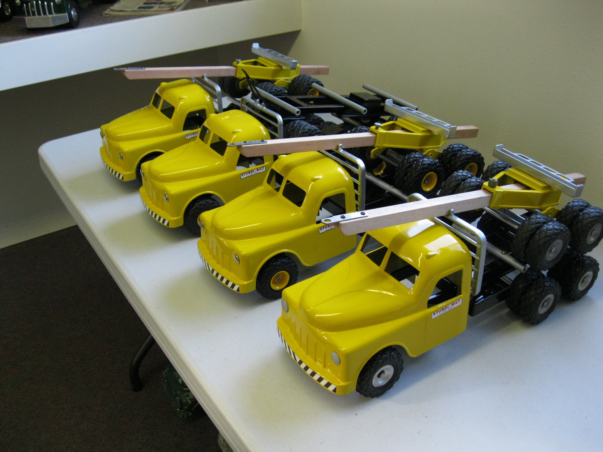Multiple yellow toy trucks with black and yellow striped bumpers and black wheels, lined up on a white table.