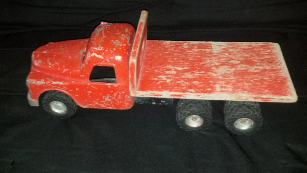 Old red toy truck with a flatbed on a black surface.