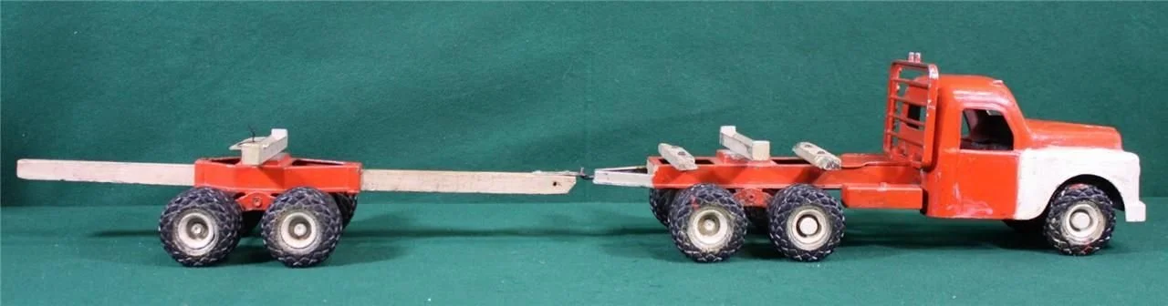 A vintage red toy truck pulling a flatbed trailer with a long wooden beam attached, on a green surface with a green background.